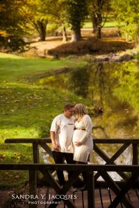 Ein Paar mit Babybauch steht auf einer Brücke in einem wunderschönen Park. ©sandra-jacques